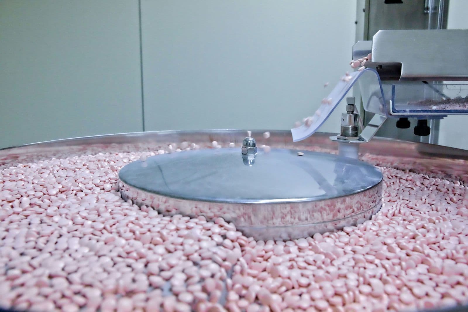 A pharmaceutical machine sorting pink tablets on a rotating stainless steel tray during production.