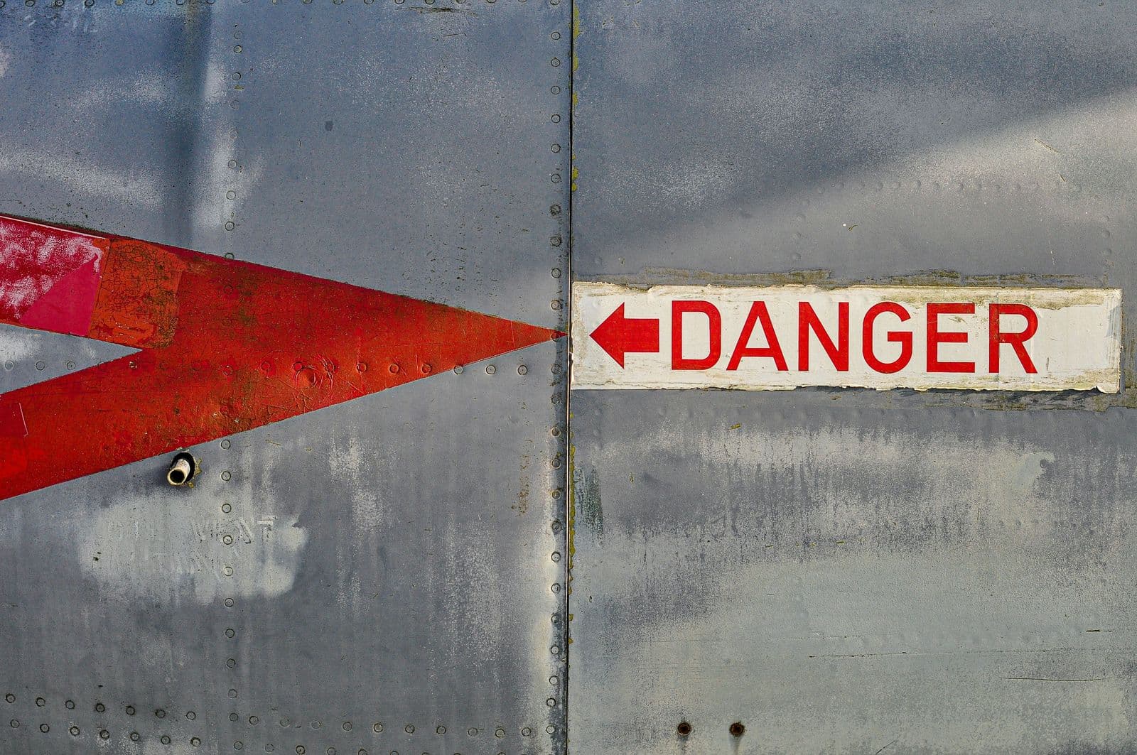 A red arrow and a "DANGER" warning label painted on a weathered, riveted metal surface.