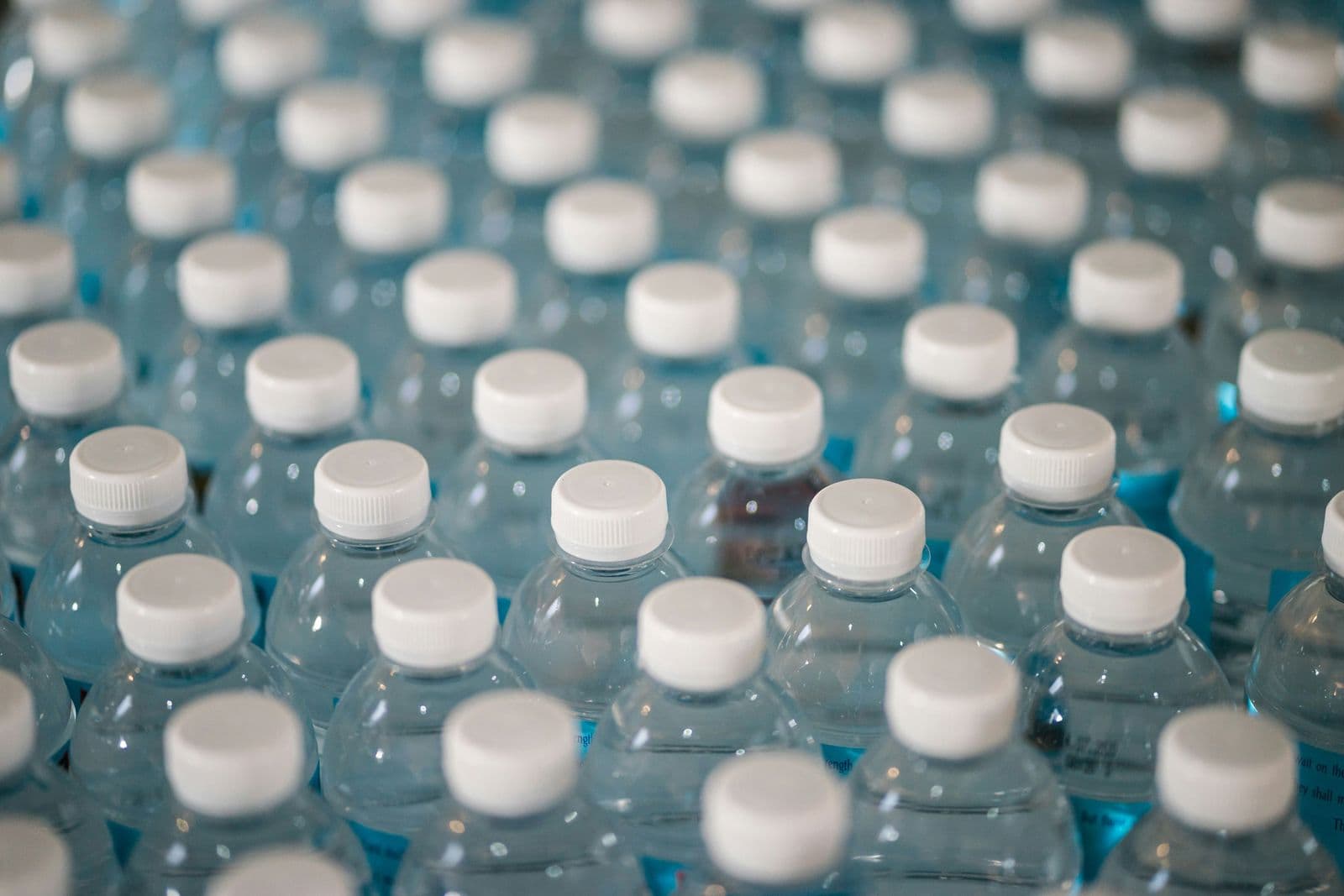 Rows of plastic mineral water bottles with white caps, seen close up.