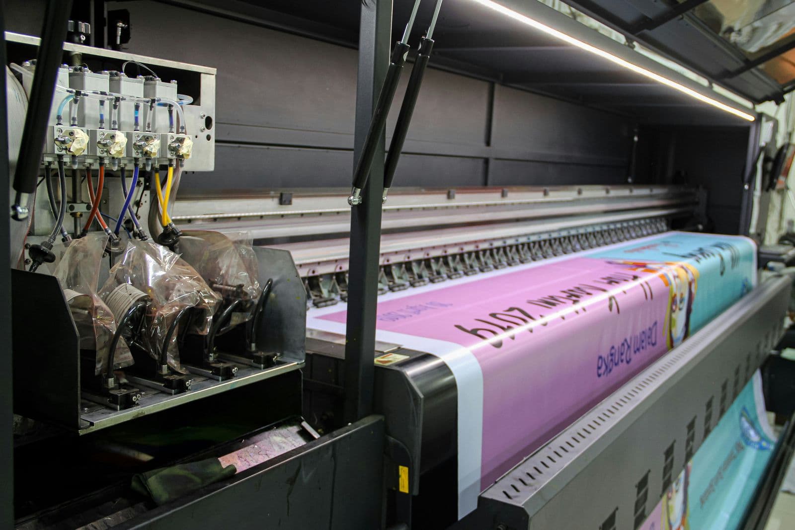 A large-format inkjet printer printing colour banners onto a wide roll of material.