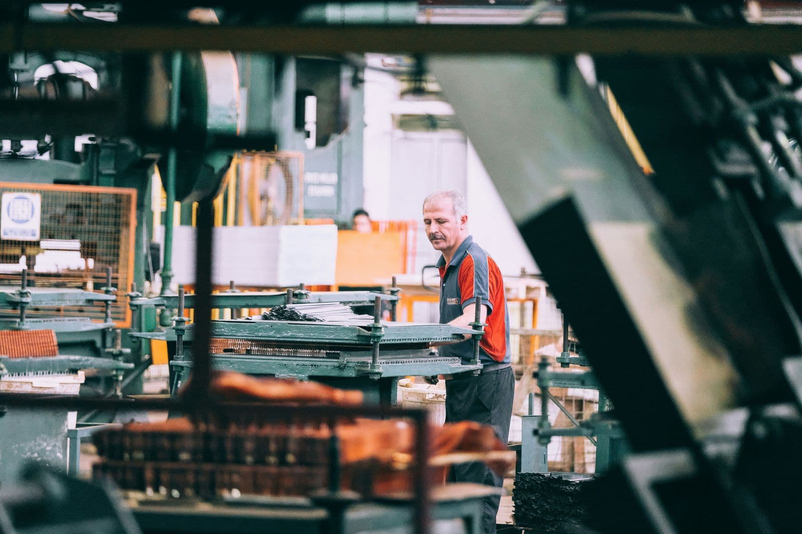 A worker operates industrial machinery on a busy factory production floor.